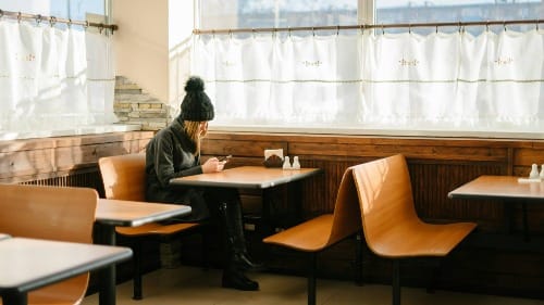 A photo of a young woman sitting alone in an empty diner. She's looking at her phone and has no food in front of her.