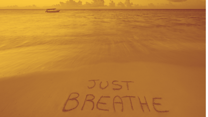 A photoof the beach with JUST BREATHE written in the sand. In tones of orange and red