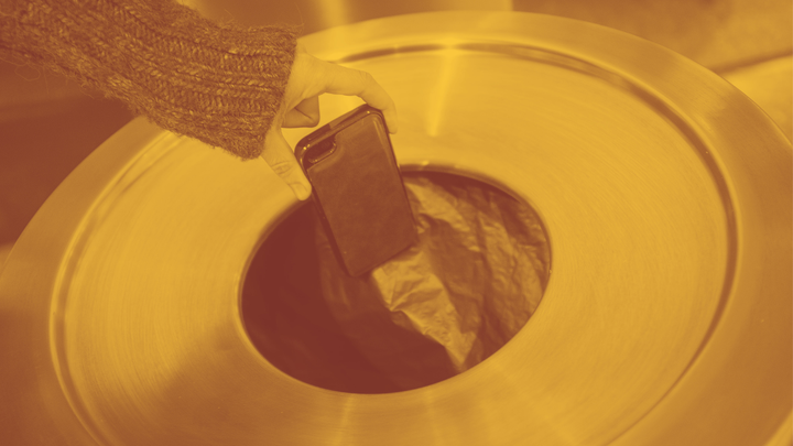 A photo of a woman's hand holding a cellphone inches above a trash can.