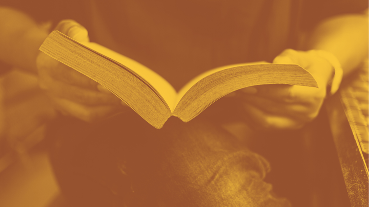 A photo of a person siting with crossed legs with an open book on their lap.