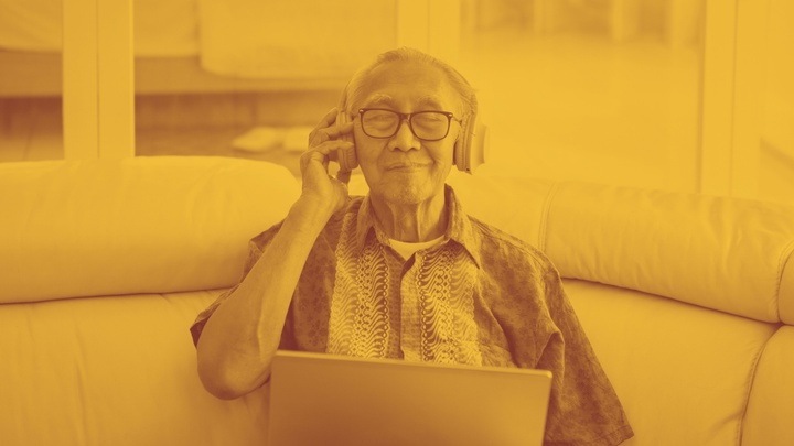 A photo of an older man looking blissful, one hand on the large headphones he's wearing.
