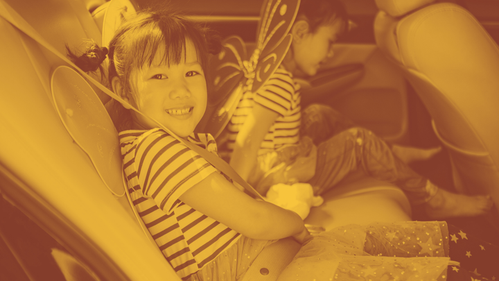 A photo of two little girls in the back seat of a car. They're wearing striped t-shirts and fairy wings.