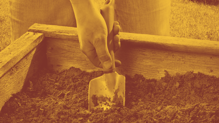 A photo of a hand holding a trowel, digging into the dirt in a planter box.