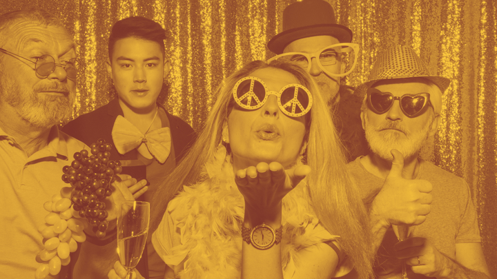 A photo of five people of various ages and races wearing wacky glasses and hats, the woman in front blowing a kiss.