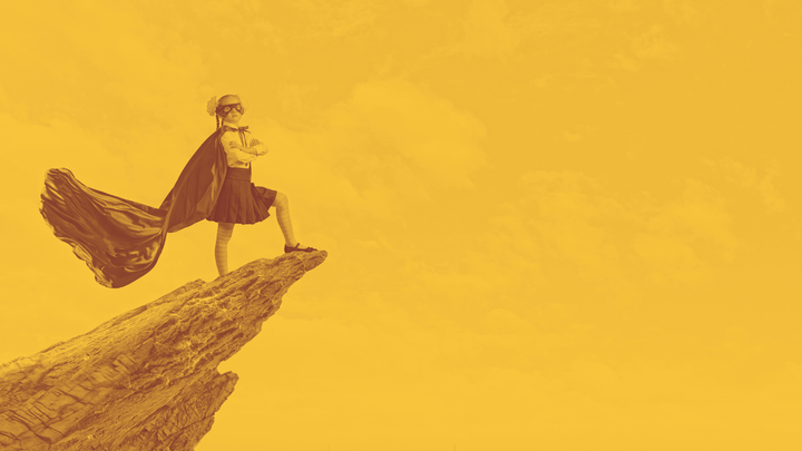 A photo of a girl in a traditional school uniform plus a ask and cape, standing defiantly on the top of a rocky outcrop against the backdrop of a cloudy sky.