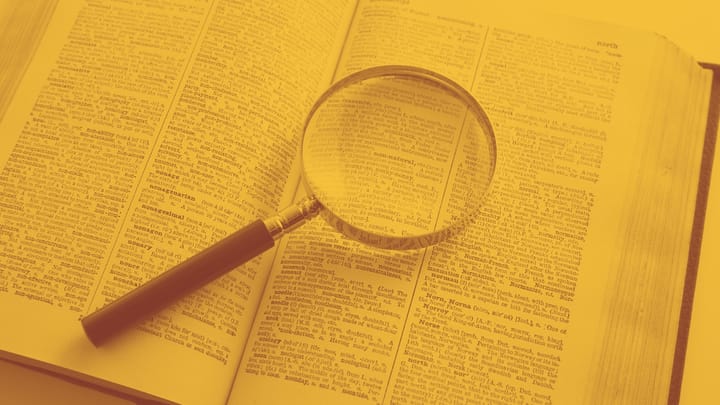 A photo of an open dictionary with a handheld magnifying glass lying across the pages.